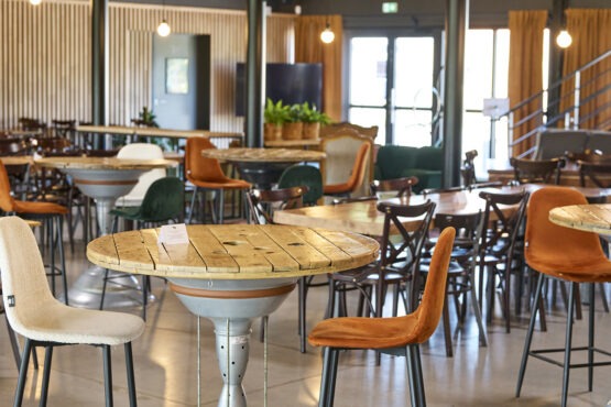 Un café spacieux et moderne, avec des tables rustiques en bois et un choix varié de sièges, notamment des fauteuils moelleux et des chaises en métal