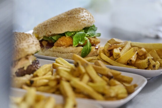 Deux assiettes avec des hamburgers et des frites sur une table. L'un des hamburgers est garni de laitue et de sauce, tandis que les assiettes sont remplies de frites dorées et croustillantes.