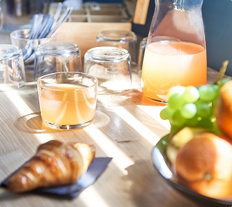 Table de petit-déjeuner avec jus, croissant et fruits dans un espace privatisable.