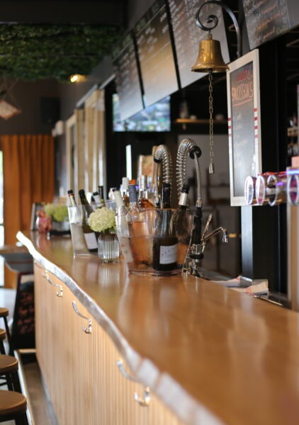 Un bar chaleureux et raffiné, doté d'un comptoir en bois incurvé, de tabourets soigneusement disposés, d'une multitude de pompes à bière, d'un éclairage d'ambiance chaleureux et de touches décoratives vertes au plafond.