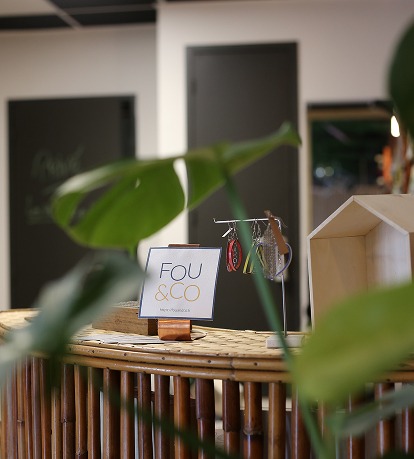 L'intérieur chaleureux du magasin, avec un comptoir en bambou sur lequel est accrochée une enseigne « FOU & CO ». 