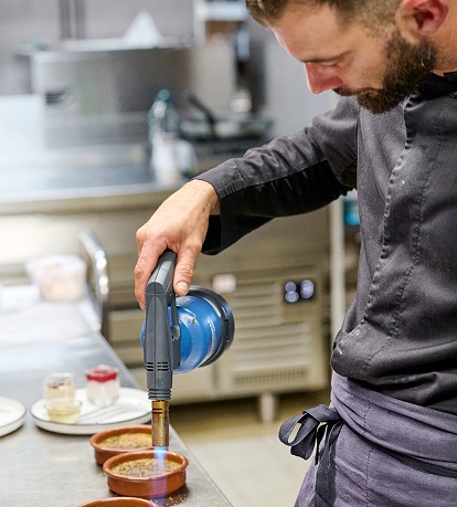 Chef caramélisant une crème brûlée avec un chalumeau, bistronomie traditionnelle