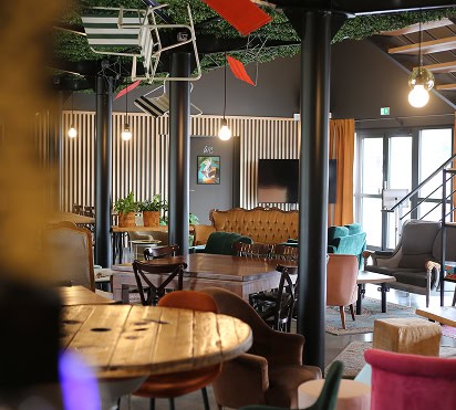 Un salon moderne et chaleureux, meublé de façon éclectique, avec notamment une table ronde en bois, des chaises colorées et un canapé en cuir.